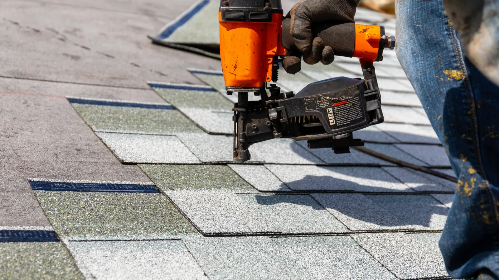New roof shingles being nailed by a pneumatic nailer